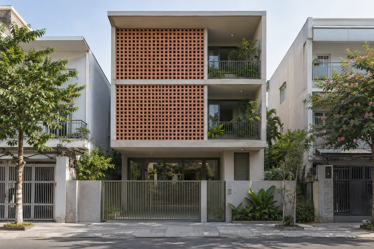Nhà phố Lam Phong – 3 tầng với gạch thông gió — Mặt tiền ba tầng với gạch thông gió đất nung ở bên trái, hai ban công lùi bên phải và cổng kim loại màu xám xanh.